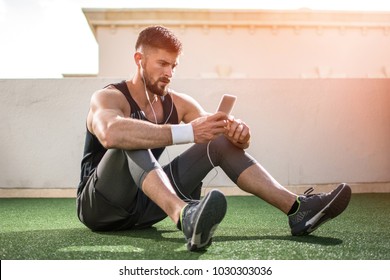 Young Handsome Man Using Phone While Having Exercise Break In Rooftop Gym.