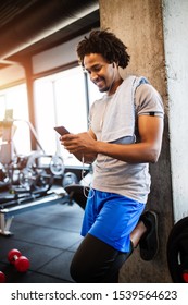 Young Handsome Man Using Phone While Having Exercise Break In Gym.