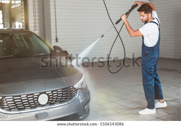 young handsome man washing car at car washing\
station using high pressure\
water