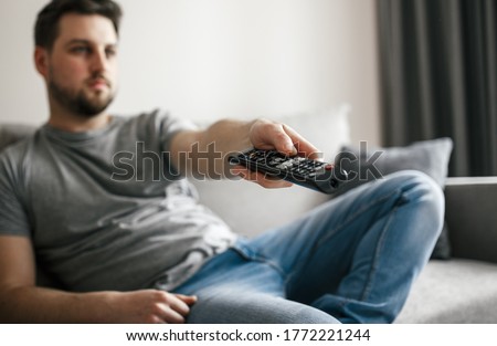 Young handsome man wathing and switching channels on tv remote control