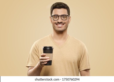 Young Handsome Man Wearing Beige T-shirt And Eyeglasses, Holding Takeaway Coffee Cup In One Hand, Satisfied With Free Time, Isolated On Brown Background