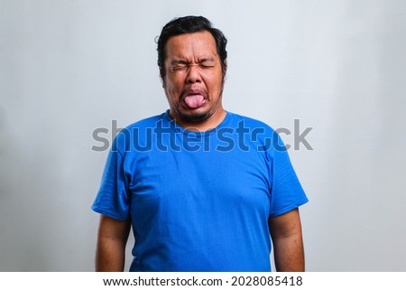 Young handsome man wearing blue shirt standing over white background sticking tongue out happy with funny expression, annoying, emotion concept