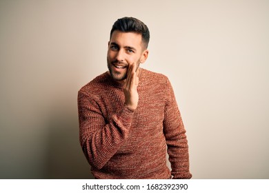 Young handsome man wearing casual sweater standing over isolated white background hand on mouth telling secret rumor, whispering malicious talk conversation