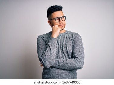 Young handsome man wearing casual sweater and glasses over isolated white background with hand on chin thinking about question, pensive expression. Smiling with thoughtful face. Doubt concept.