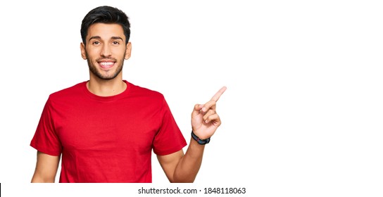 Young Handsome Man Wearing Casual Red Tshirt With A Big Smile On Face, Pointing With Hand Finger To The Side Looking At The Camera. 