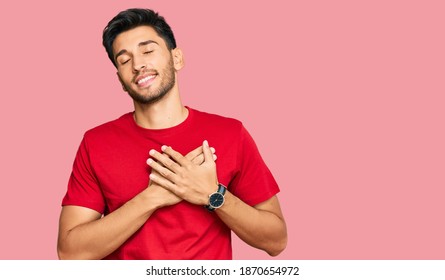 Young Handsome Man Wearing Casual Red Tshirt Smiling With Hands On Chest With Closed Eyes And Grateful Gesture On Face. Health Concept. 