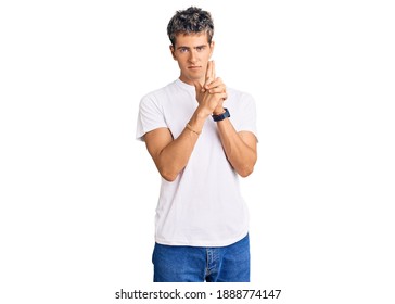 Young Handsome Man Wearing Casual White Tshirt Holding Symbolic Gun With Hand Gesture, Playing Killing Shooting Weapons, Angry Face 