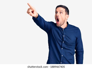 Young handsome man wearing casual shirt pointing with finger surprised ahead, open mouth amazed expression, something on the front 