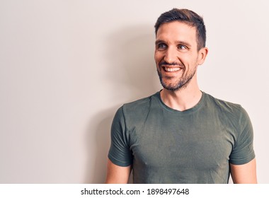 Young Handsome Man Wearing Casual T-shirt Standing Over Isolated White Background Looking To Side, Relax Profile Pose With Natural Face And Confident Smile.