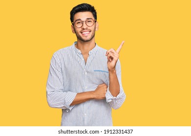 Young handsome man wearing casual clothes and glasses with a big smile on face, pointing with hand and finger to the side looking at the camera. 