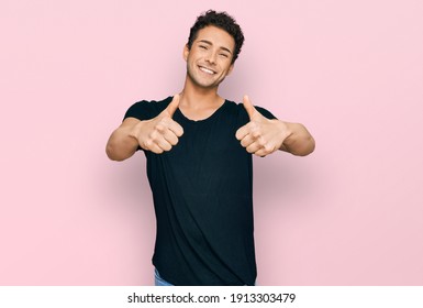 Young Handsome Man Wearing Casual Black T Shirt Approving Doing Positive Gesture With Hand, Thumbs Up Smiling And Happy For Success. Winner Gesture. 