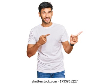 Young handsome man wearing casual white tshirt smiling and looking at the camera pointing with two hands and fingers to the side.  - Shutterstock ID 1933965227
