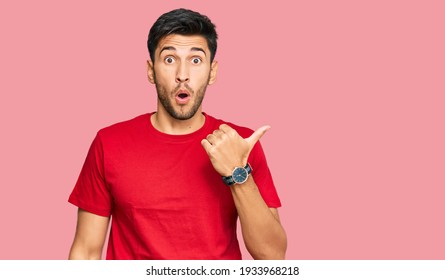 Young handsome man wearing casual red tshirt surprised pointing with hand finger to the side, open mouth amazed expression. 