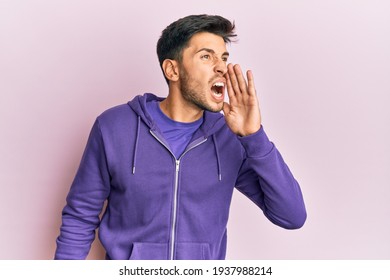 Young handsome man wearing casual sweatshirt shouting and screaming loud to side with hand on mouth. communication concept. 
