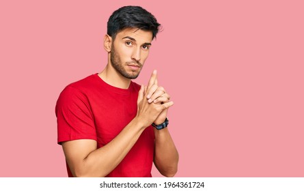 Young Handsome Man Wearing Casual Red Tshirt Holding Symbolic Gun With Hand Gesture, Playing Killing Shooting Weapons, Angry Face 