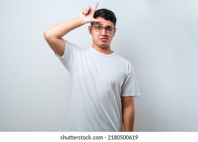 Young handsome man wearing casual shirt standing over white isolated background making fun of people with fingers on forehead doing loser gesture mocking and insulting. - Shutterstock ID 2180500619