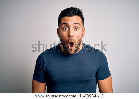 Young handsome man wearing casual t-shirt standing over isolated white background afraid and shocked with surprise expression, fear and excited face.