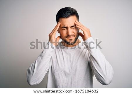 Young handsome man wearing casual t-shirt standing over isolated white background suffering from headache desperate and stressed because pain and migraine. Hands on head.