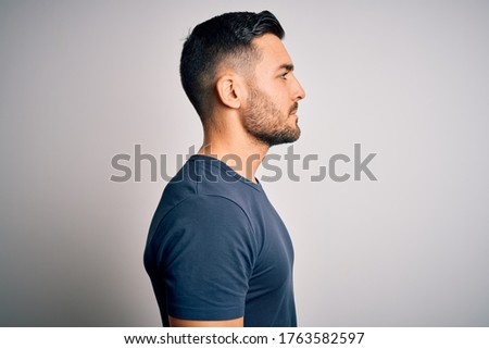 Young handsome man wearing casual t-shirt standing over isolated white background looking to side, relax profile pose with natural face with confident smile.