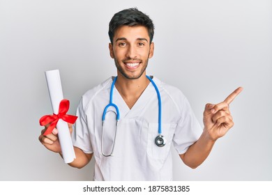 Young Handsome Man Wearing Doctor Uniform Holding Medical Degree Smiling Happy Pointing With Hand And Finger To The Side 