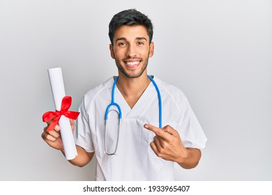 Young Handsome Man Wearing Doctor Uniform Holding Medical Degree Smiling Happy Pointing With Hand And Finger 