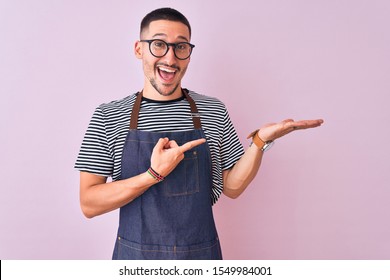 Young handsome man wearing employee apron over isolated background amazed and smiling to the camera while presenting with hand and pointing with finger.