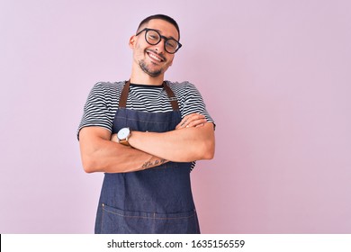 Young handsome man wearing employee apron over isolated background happy face smiling with crossed arms looking at the camera. Positive person.