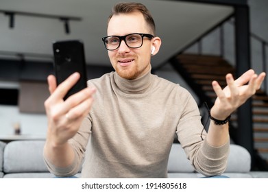 A young handsome man wearing eyeglasses using a smartphone for video chat, video call. A smiling guy is talking online via video connection on the cellphone - Shutterstock ID 1914805618