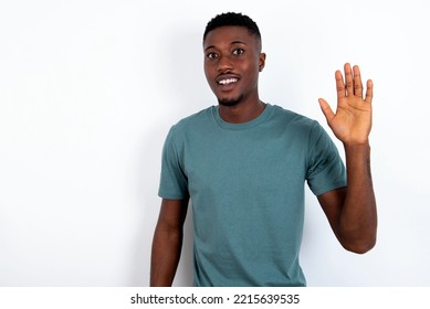 Young Handsome Man Wearing Green T-shirt Over White Background Waiving Saying Hello Or Goodbye Happy And Smiling, Friendly Welcome Gesture.