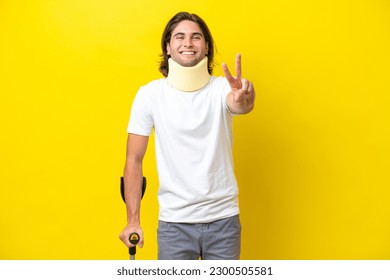 Young handsome man wearing neck brace and crutches isolated on yellow background smiling and showing victory sign - Powered by Shutterstock