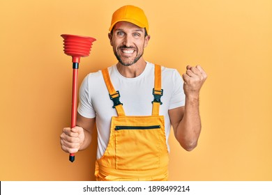 Young handsome man wearing plumber uniform holding toilet plunger screaming proud, celebrating victory and success very excited with raised arm 