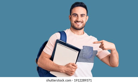 Young handsome man wearing student backpack and notebook pointing finger to one self smiling happy and proud 