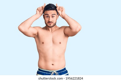 Young Handsome Man Wearing Swimwear Doing Funny Gesture With Finger Over Head As Bull Horns 