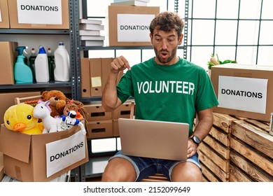 Young Handsome Man Wearing Volunteer T Shirt Using Laptop Pointing Down With Fingers Showing Advertisement, Surprised Face And Open Mouth 