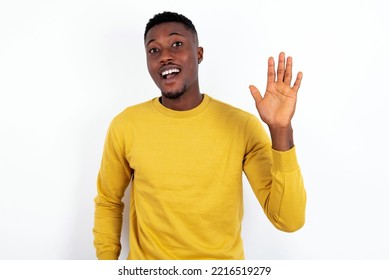 Young Handsome Man Wearing Yellow Sweater Over White  Background Waiving Saying Hello Or Goodbye Happy And Smiling, Friendly Welcome Gesture.