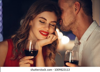 Young handsome man whisper to his gorgeous woman while have romantic dinner and drinking wine on valentines day