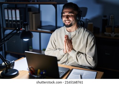 Young Handsome Man Working Using Computer Laptop At Night Praying With Hands Together Asking For Forgiveness Smiling Confident. 