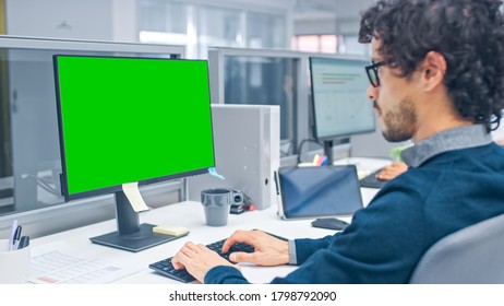 Young Handsome Manager With Curly Hair Works On A Desktop Computer With Green Screen Mock Up. Diverse And Motivated Business People Work On Computers In Modern Open Office.