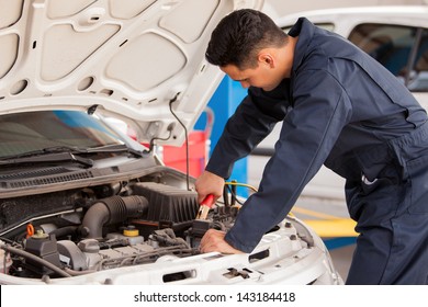 Young handsome mechanic putting some jumper cables on a battery before jump starting it - Powered by Shutterstock