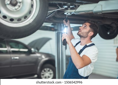 Young Handsome Mechanic Working In Car Service Department Fixing Vehicle Chassis