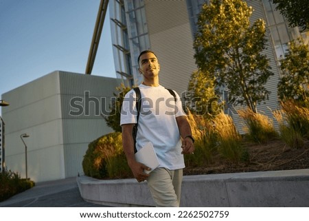 Young handsome middle eastern student with laptop walking in university campus, copy space. Education concept 