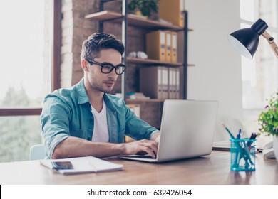 Young handsome minded man in jeans shirt and spectacles sitting at the table and typink a letter to his  acquaintance - Powered by Shutterstock