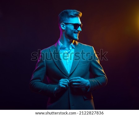 Young handsome model posing in a studio in a trendy neon light. Fashionable man in a stylish suit. Vibrant color. Bright colorful light effects. Disco style. Overlay. Gel filter. Supersaturated