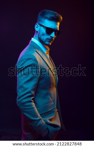 Young handsome model posing in a studio in a trendy neon light. Fashionable man in a stylish suit. Vibrant color. Bright colorful light effects. Disco style. Overlay. Gel filter. Supersaturated