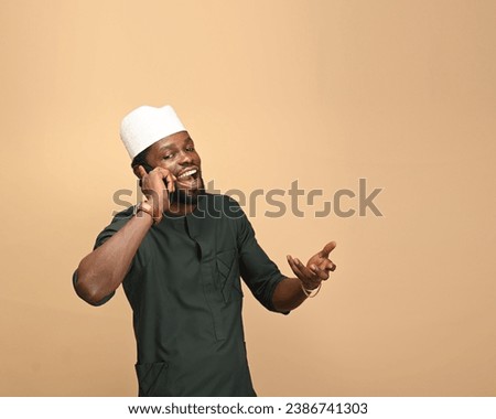 Young handsome Nigerian Hausa business man in an Africa traditional outfit reacting to his lover's woes on mobile call. Young ambitious businessman. Copy space