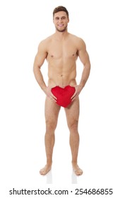 Young handsome nude man covering his self with heart pillow.