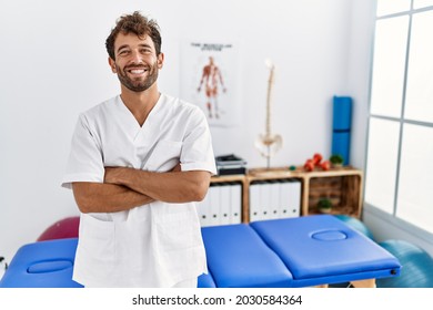 Young handsome physiotherapist man working at pain recovery clinic happy face smiling with crossed arms looking at the camera. positive person.  - Shutterstock ID 2030584364