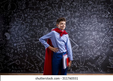 Young Handsome School Boy With Red Cape In Front Of Big Blackboard