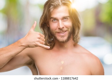 Young handsome shirtless man with long hair showing sexy body over isolated background smiling doing phone gesture with hand and fingers like talking on the telephone. Communicating concepts. - Shutterstock ID 1188817642