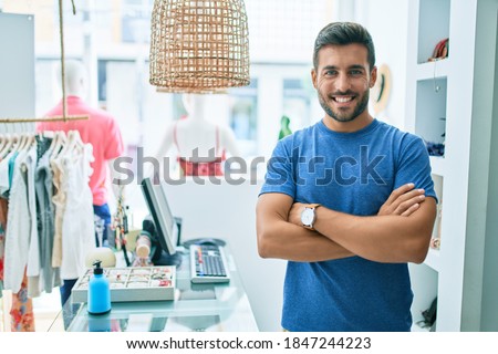 Young handsome shopkeeper smiling happy standing at clothing store